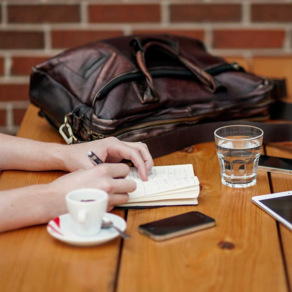 Twee mensen overleggen aan tafel met een notitieboekje, koffie en een tablet