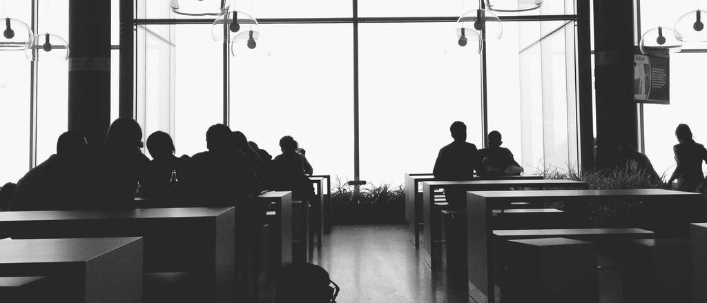 Cursisten aan tafels in een lichte cafetaria met grote ramen