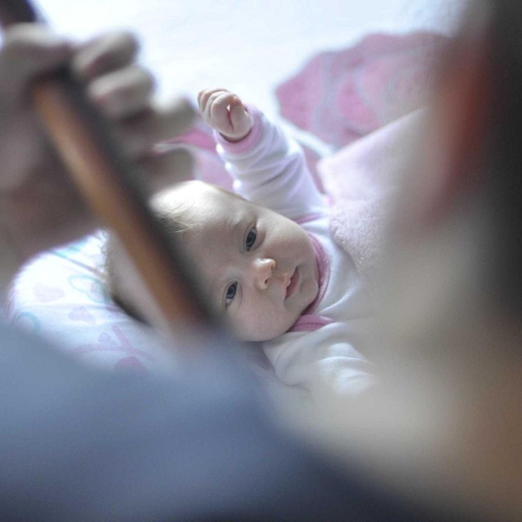 Een baby in een roze pakje ligt op een dekentje en kijkt op naar een volwassene
