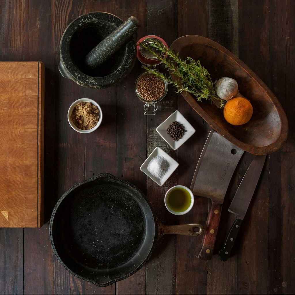 Snijplank, vijzel, kruiden en een gietijzeren pan op een houten keukentafel