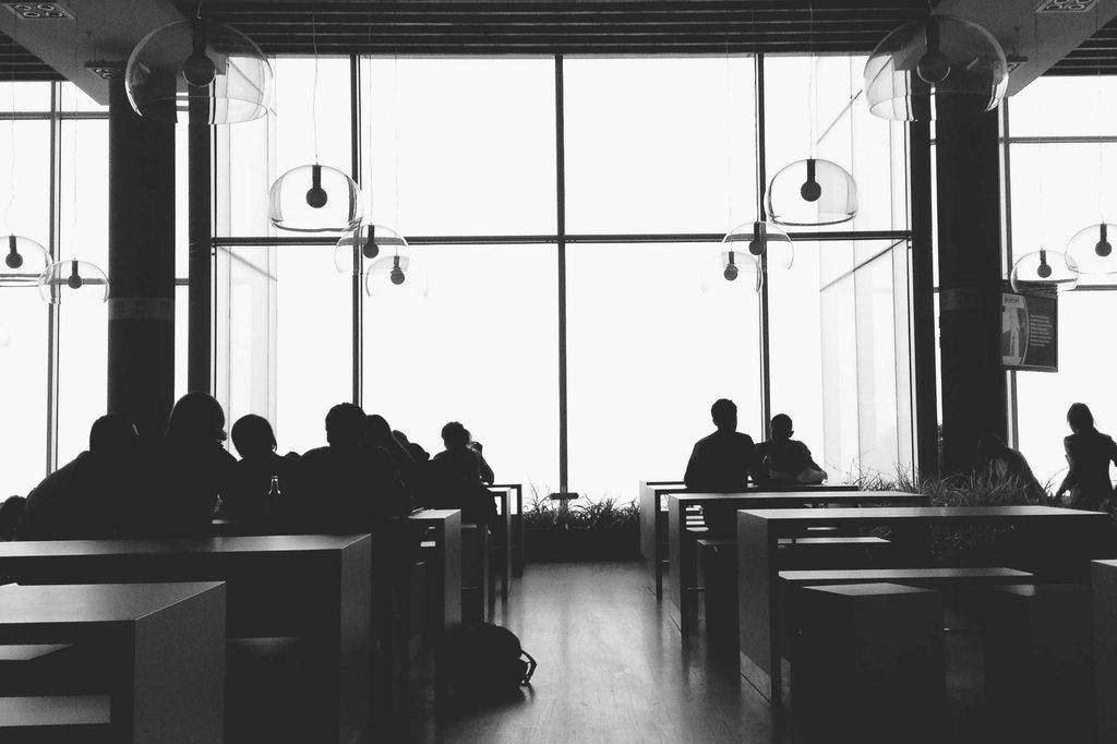 Cursisten aan tafels in een lichte cafetaria met grote ramen