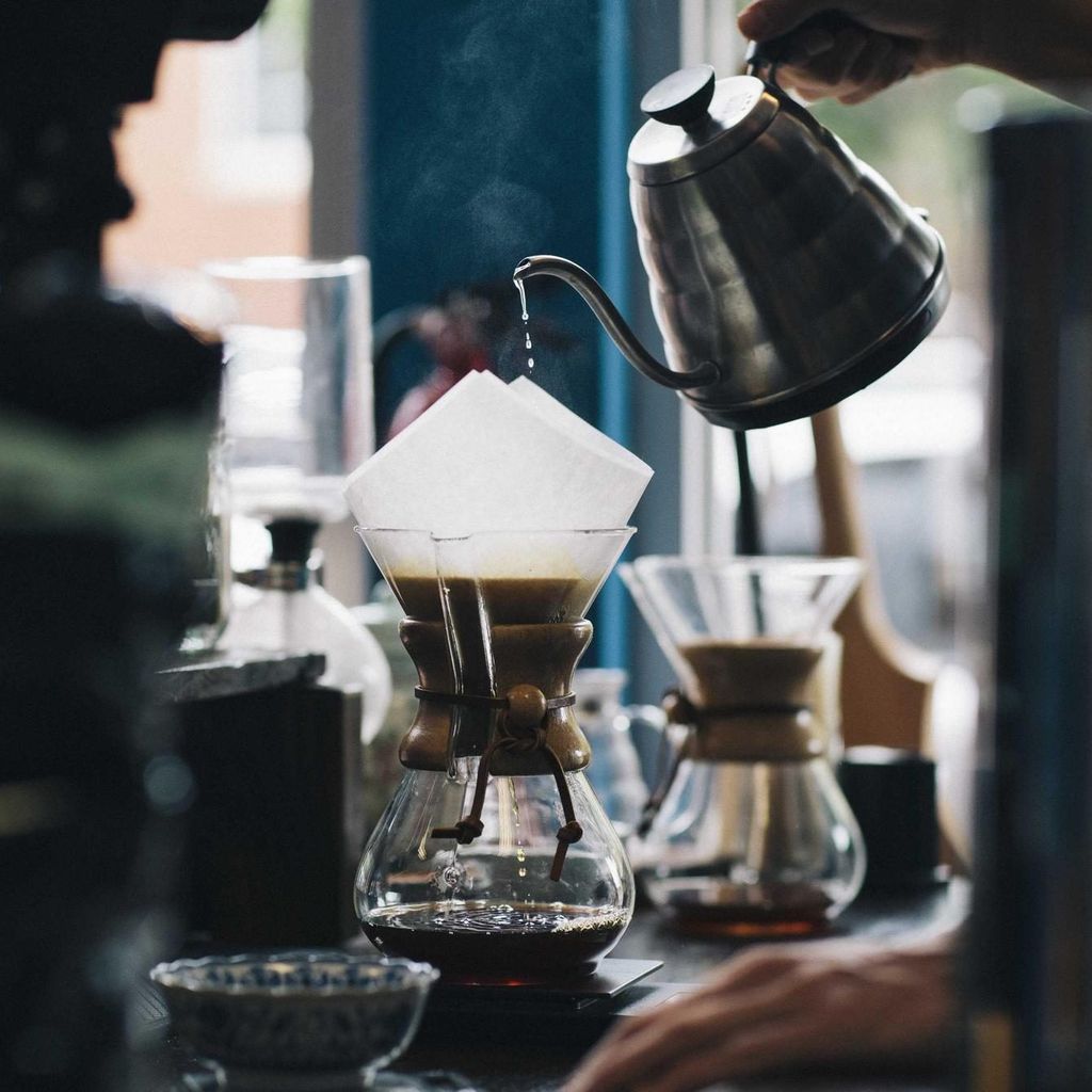 Een barista giet heet water over koffie in een glazen filterkan