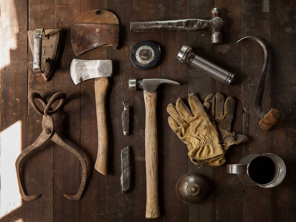 Oud handgereedschap op een donkere houten werkbank: hamer, bijl, nijptang en werkhandschoenen